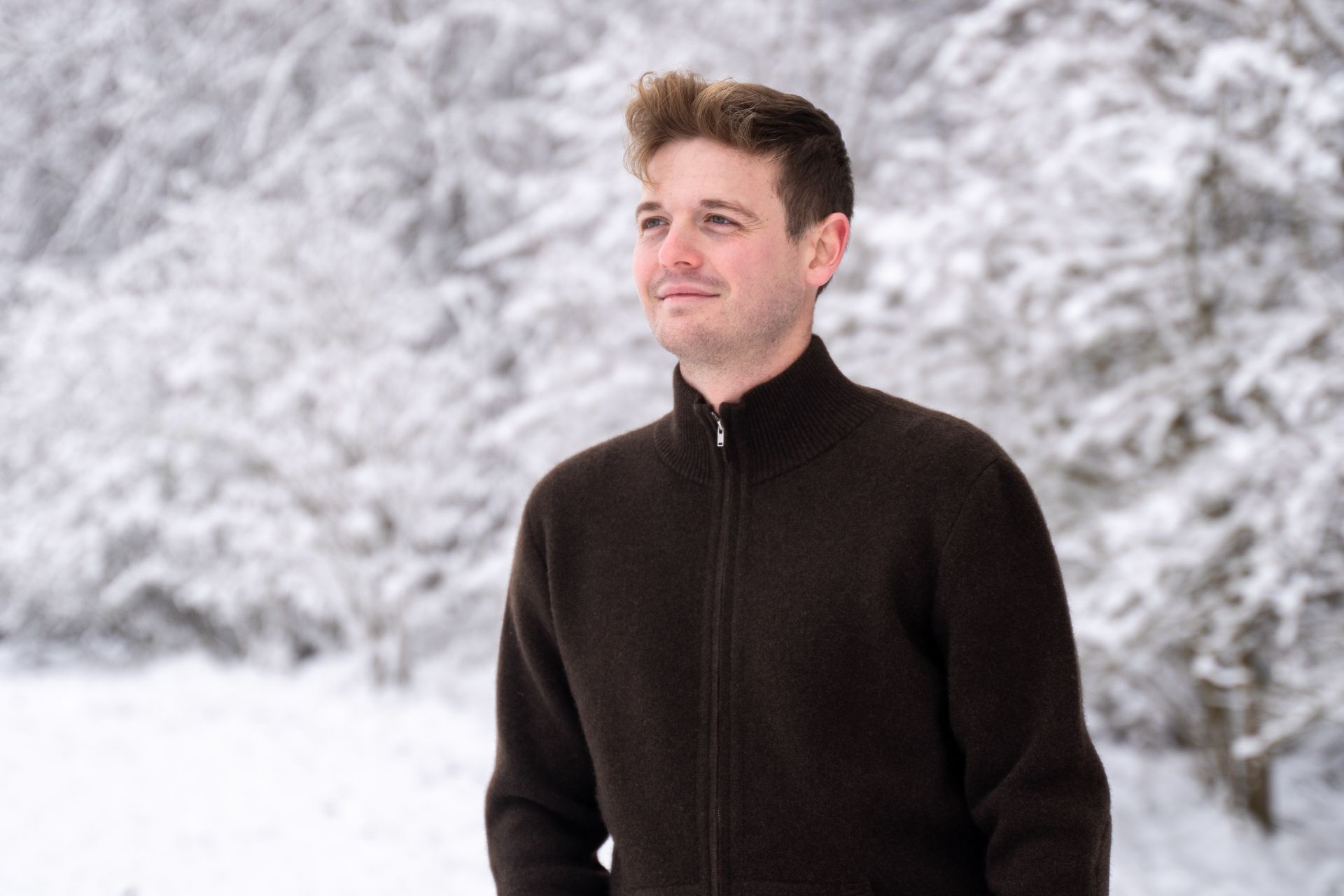 Die Strickjacke aus Yakhaar hält dich im Winter zuverlässig warm Junger Mann steht in dunkler Strickjacke vor schneebedecktem Wald