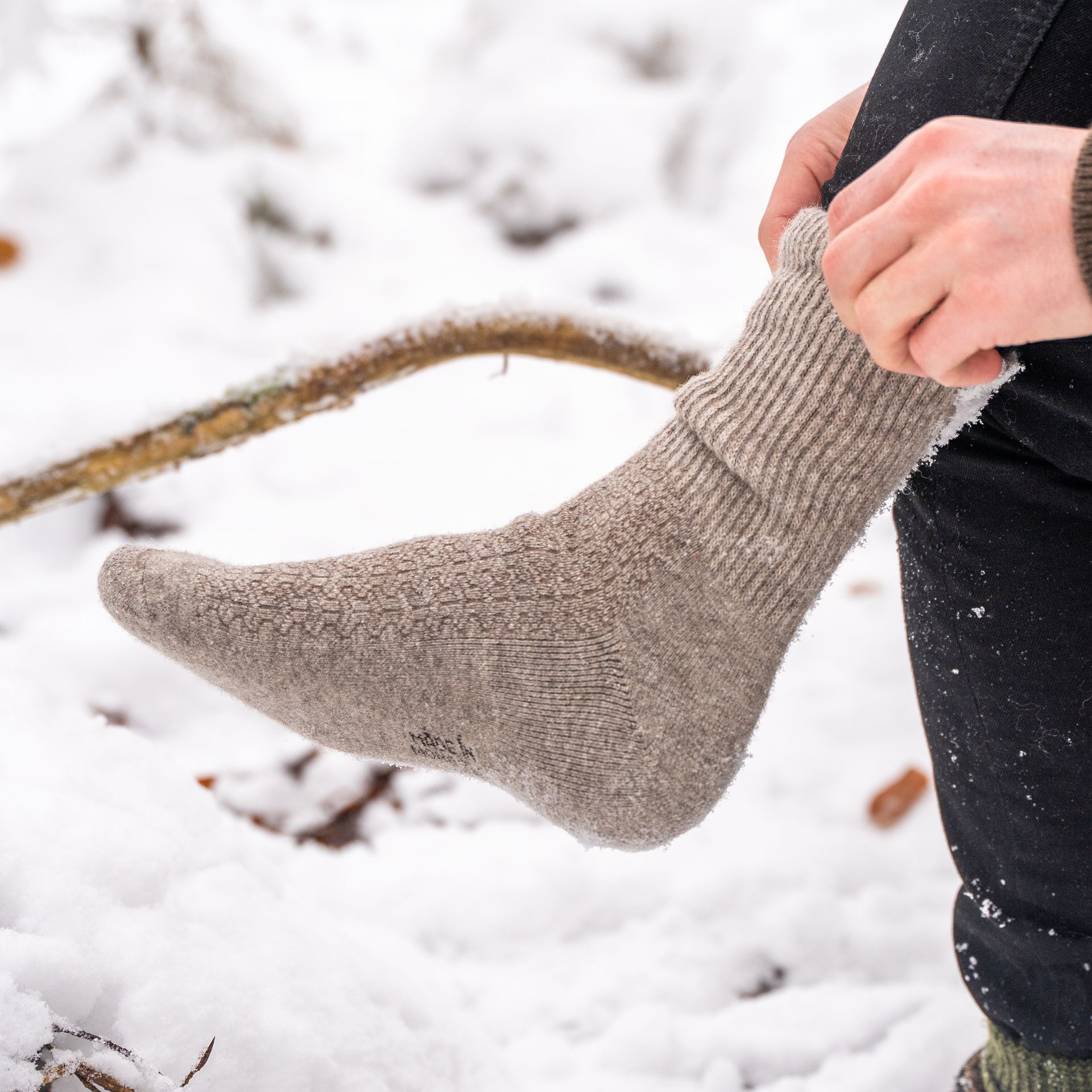 Graue Wollsocken für jede Wetterlage Naturgraue Socken werden in einer schneebedeckten Landschaft angezogen