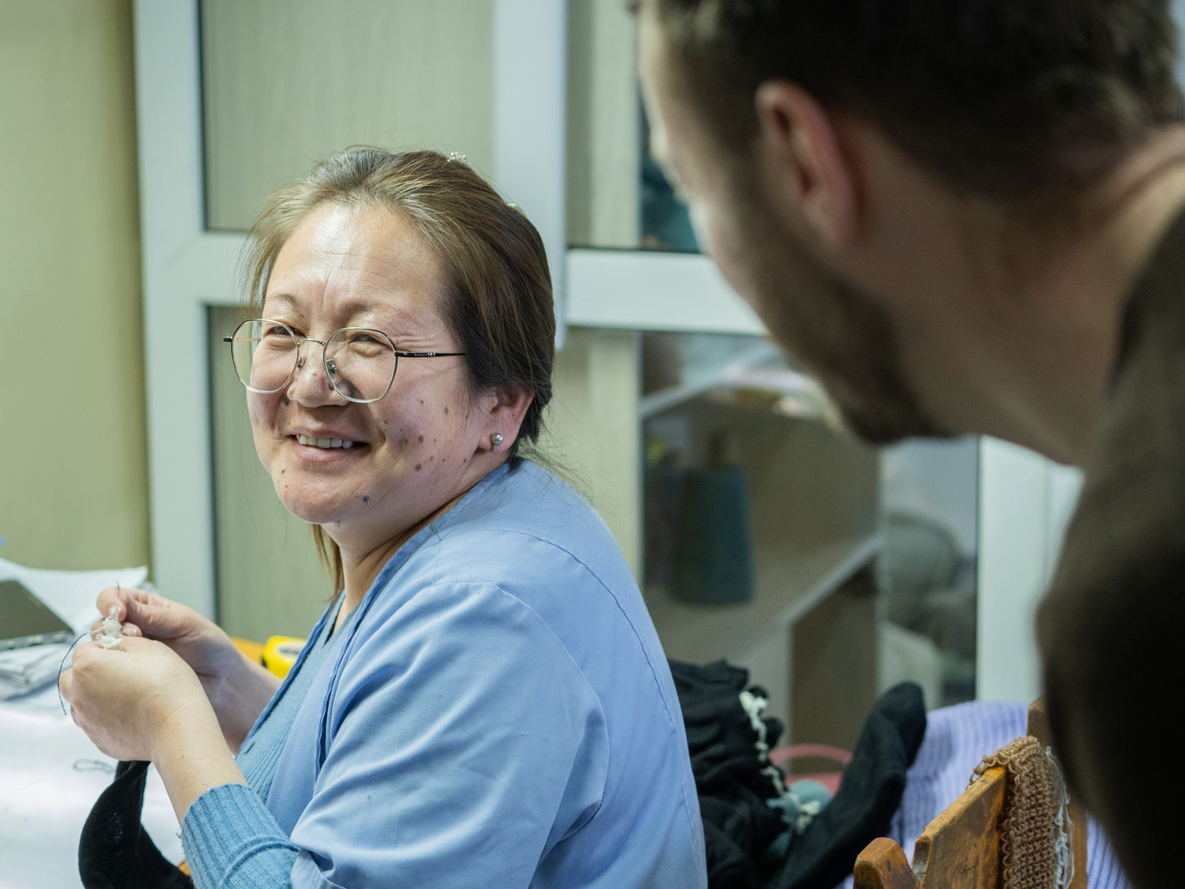 In der Mongolei werden einige Produktionsschritte per Hand genäht Eine Frau lacht in die Kamera und arbeitet an einem Kleidungsstück in der Mongolei