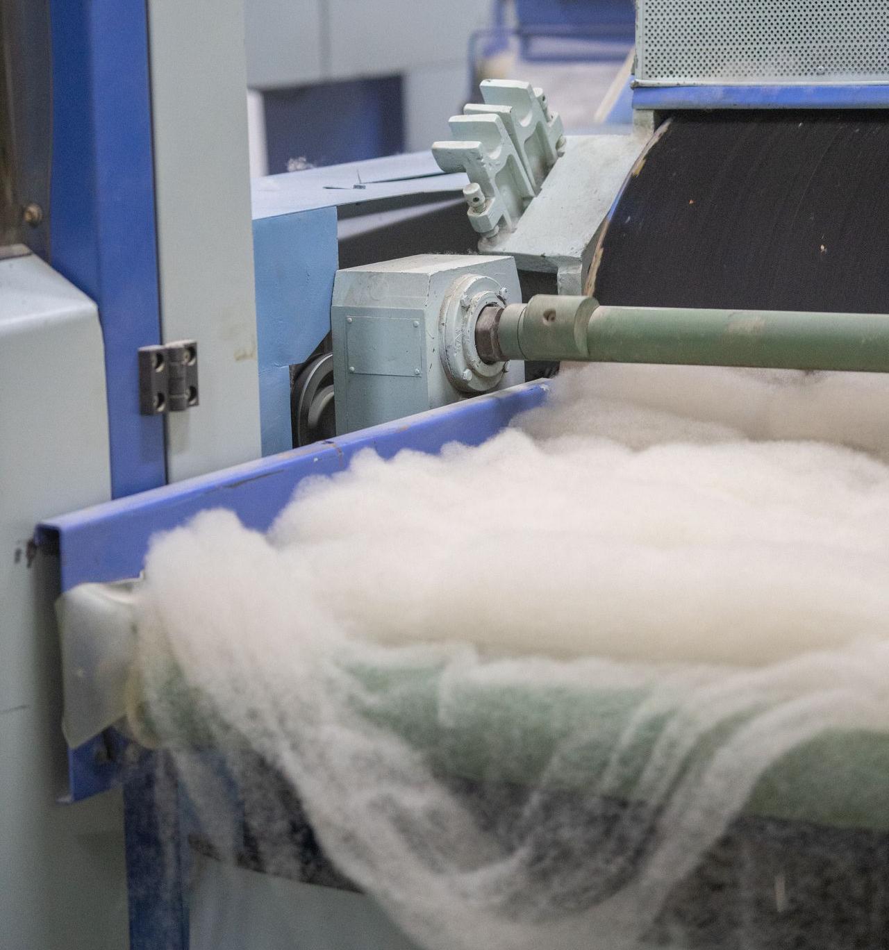 Bevor die Wolle gesponnen wird muss ein gleichmäßiges Wollvlies produziert werden In einer Produktionshalle wird mittels Maschinen ein Wollfvlies zur weiteren Verarbeitung produziert
