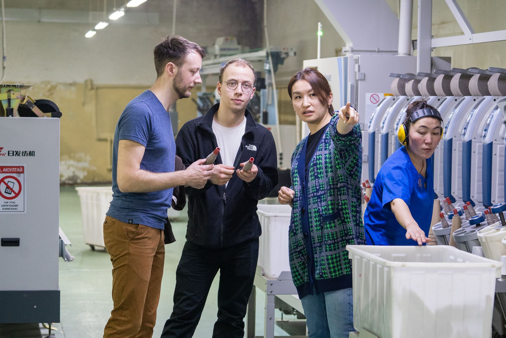 Malte, Lennart und Otgoo in den Produktionshallen 2022 Mehrere Personen stehen in einer Produktionshalle. Eine Frau erklärt den anderen wie die Produktion funktioniert.