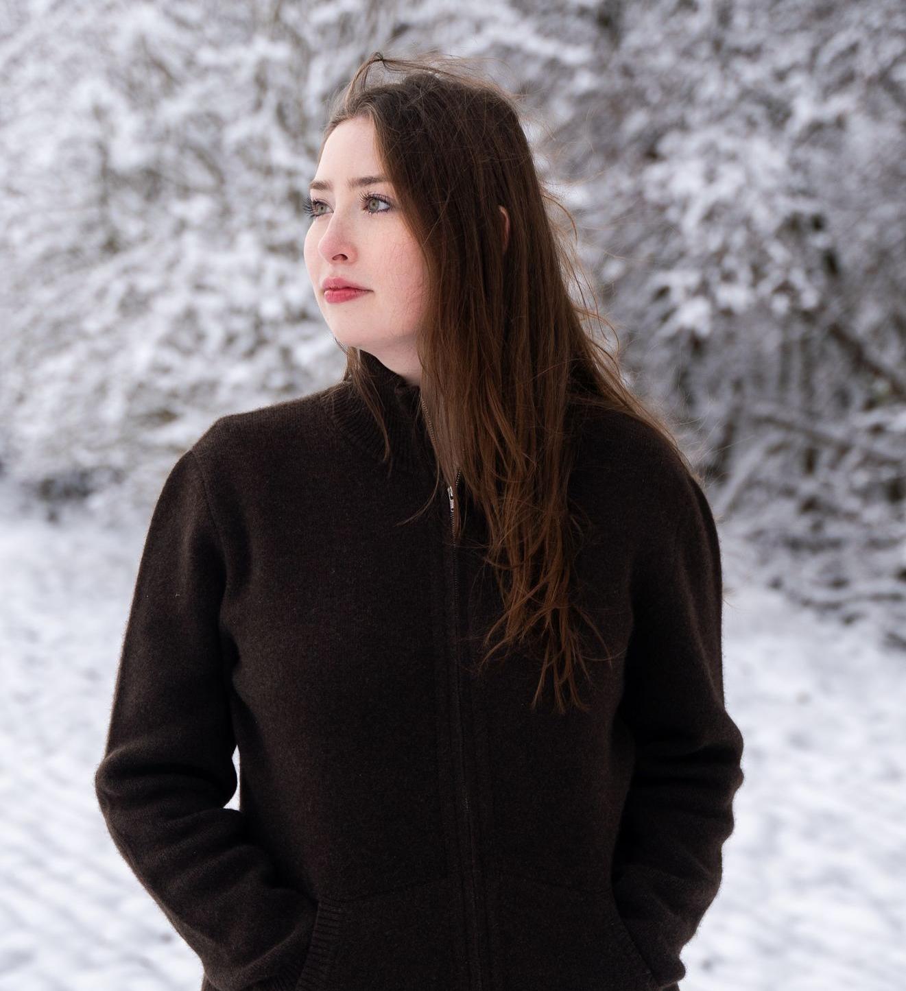 Modell steht in Schneelandschaft und trägt dunkelbraune Strickjacke aus Yakhaar