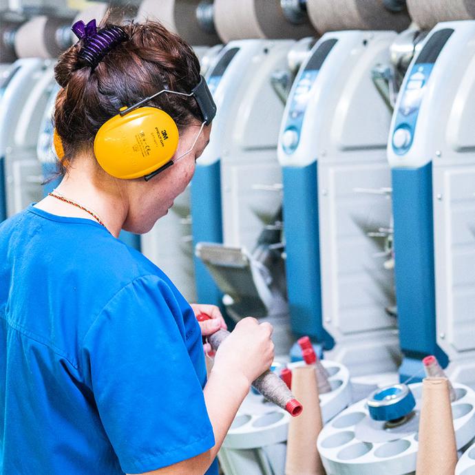 Arbeitssicherheit ist in der Textilproduktion essenziell Ein Bild einer Frau vor Textilmaschinen, die gelbe Ohrschützer trägt