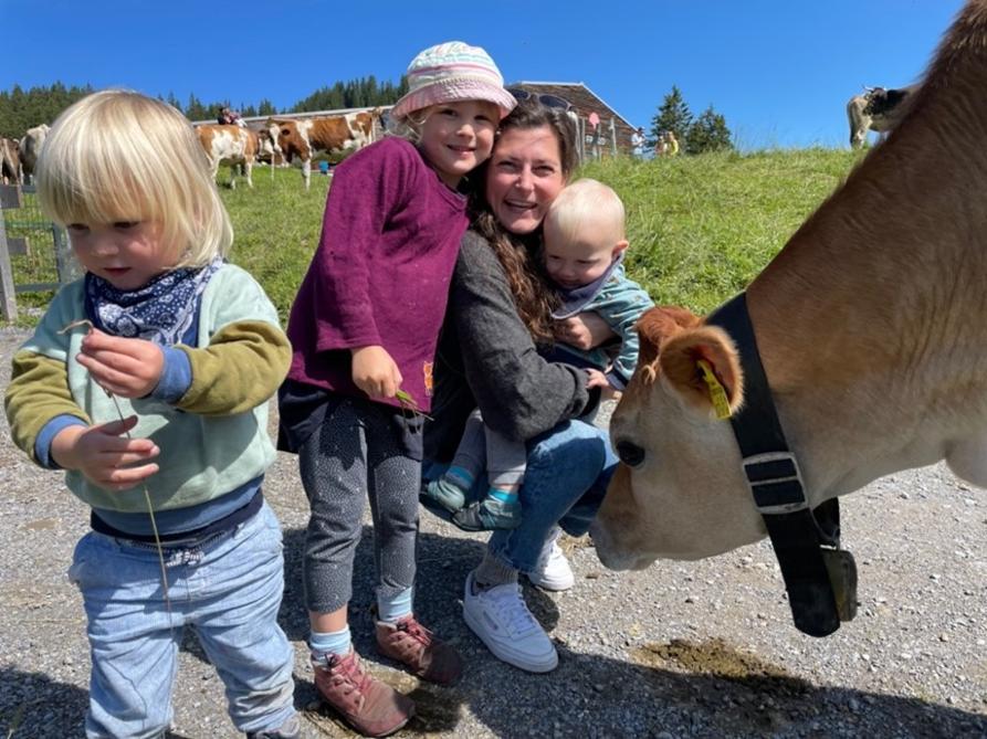 Lisa versorgt seit langem Klein und Groß mit Wollsocken Eine junge Frau mit drei Kindern neben einer schnuppernden Kuh