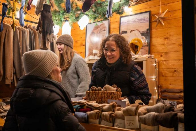 Besucher in Winterkleidung, die sich an einem gut besuchten Weihnachtsmarktstand umsehen.