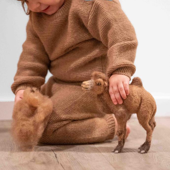 Toddler in soft camel wool jumper playing with a toy camel.