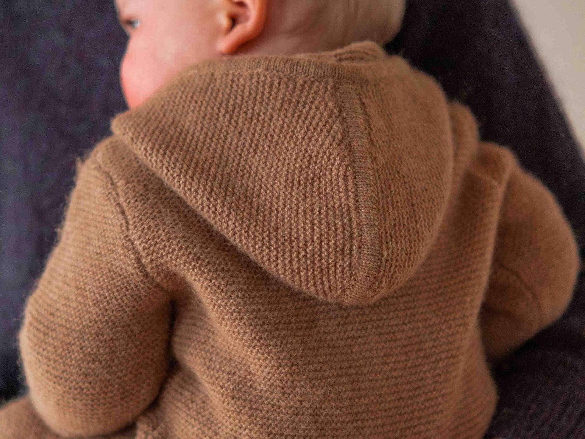 Baby Overall aus Kamelwolle hält warm und weich Baby mit braunem Wolloverall aus Kamelwolle wird in den Armen gehalten