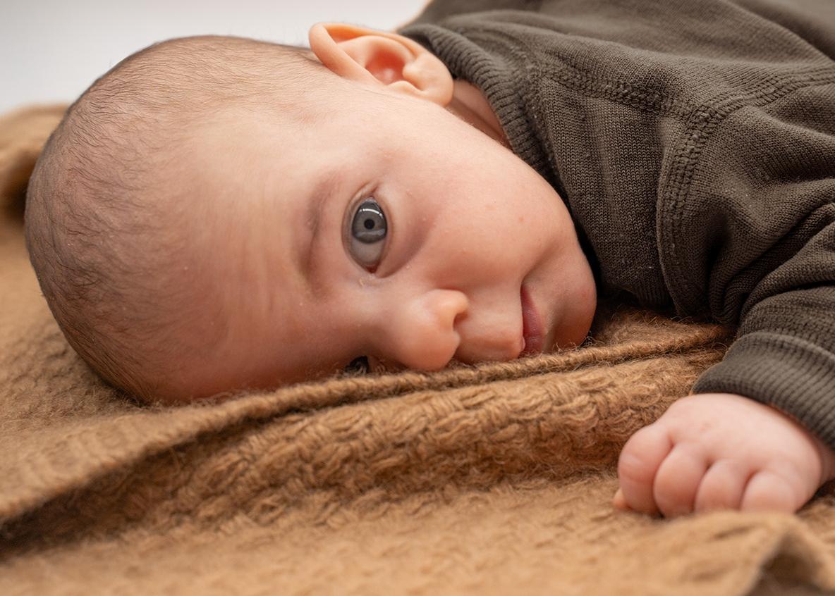 Kuschelige Wolldecke für Babys aus Kamelwolle Ein Baby liegt auf einer braunen Wolldecke für Babys und schaut wach in die Kamera
