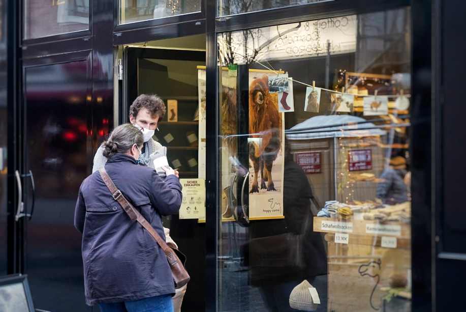 Ein Mann mit Maske verkauft einer Frau vor einem Laden ein paar Wollsocken