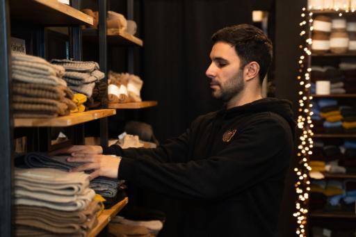 Ein schwarzhaariger Mann sortiert ein Regal mit Wollkleidung
