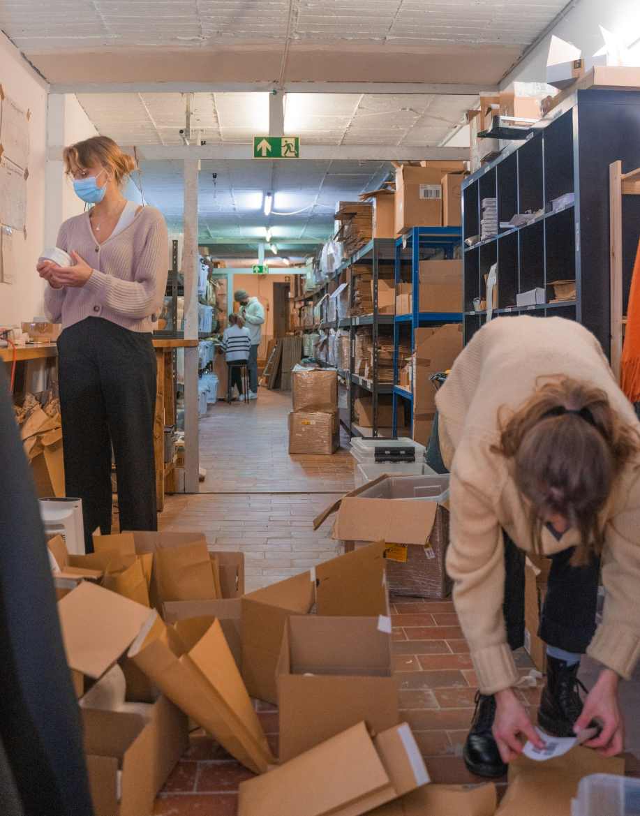 Menschen zwischen Paketen in einem Lagergang mit Maske auf dem Mund