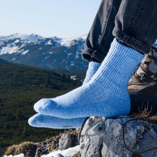 Wollsocken für Unterwegs, Zuhause und im Bett Eisblaue Wollsocken werden vor einem Bergpanorama getragen an Füßen auf einem Stein