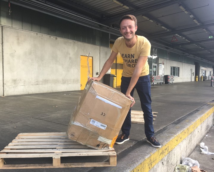 Ein junger Mann freut sich über ein Paket, dass auf einer Palette liegt.