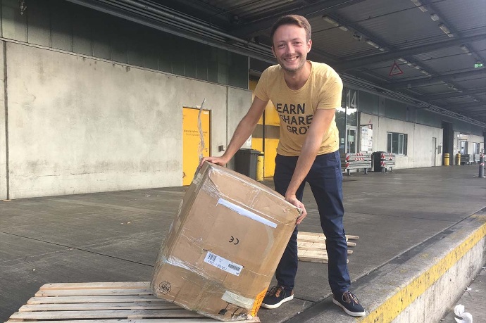 Malte empfängt 2015 das erste große Paket Ein junger Mann kippt ein großes Paket auf der Ladefläche einer Abholstation.