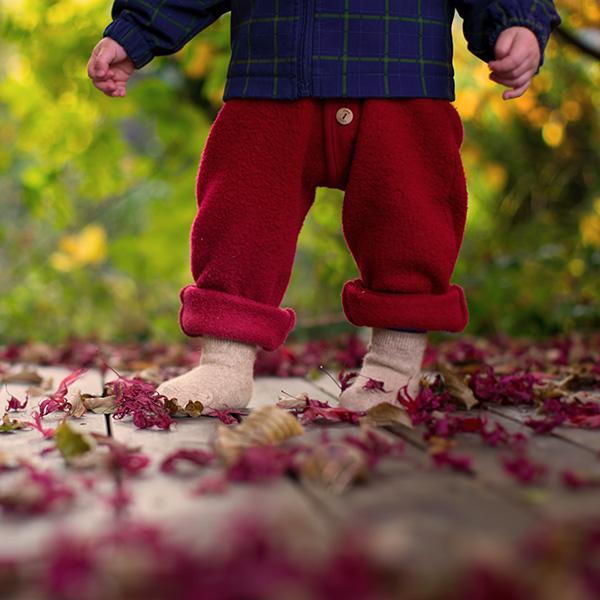 Kindersocken aus Kamelwolle Ein Kleinkind läuft mit Socken über Holzboden voller roter Blätter