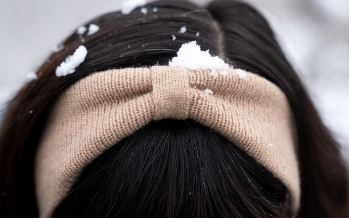 Beiges Stirnband mit Schnee zwischen schwarzen Haaren